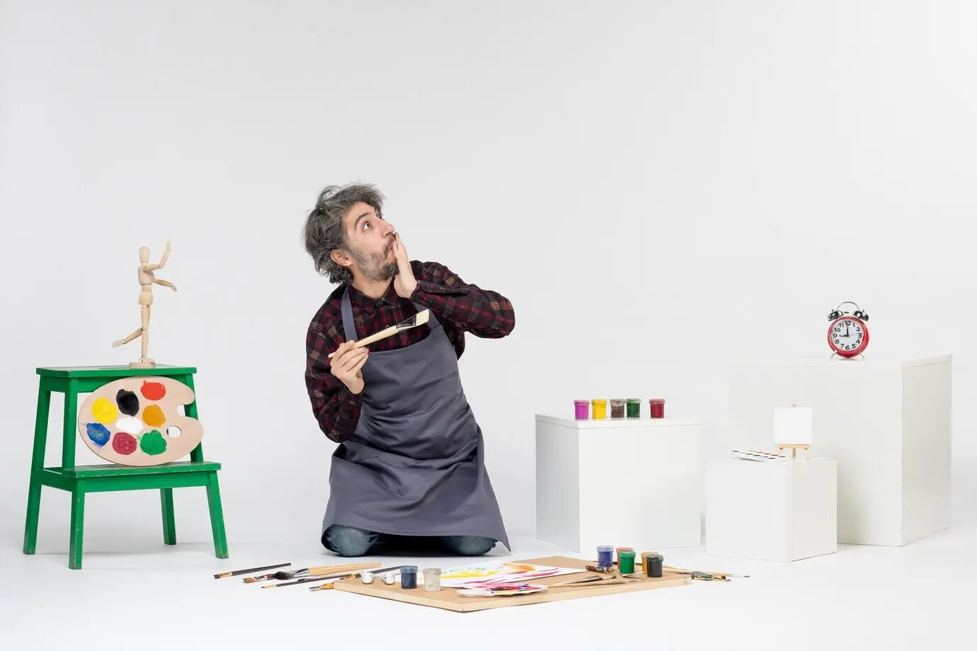 Vorderansicht eines männlichen Malers und Künstlers in einem Raum, vor weißem Hintergrund, mit Farben und Pinseln zum Malen und Zeichnen eines farbigen Bildes.