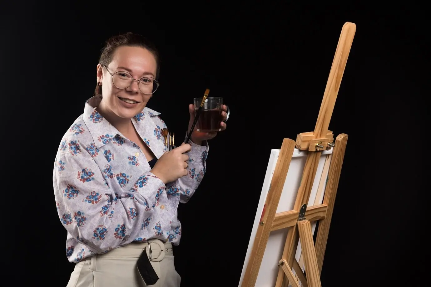 Künstlerin hält Pinsel und Leinwand vor schwarzem Hintergrund.