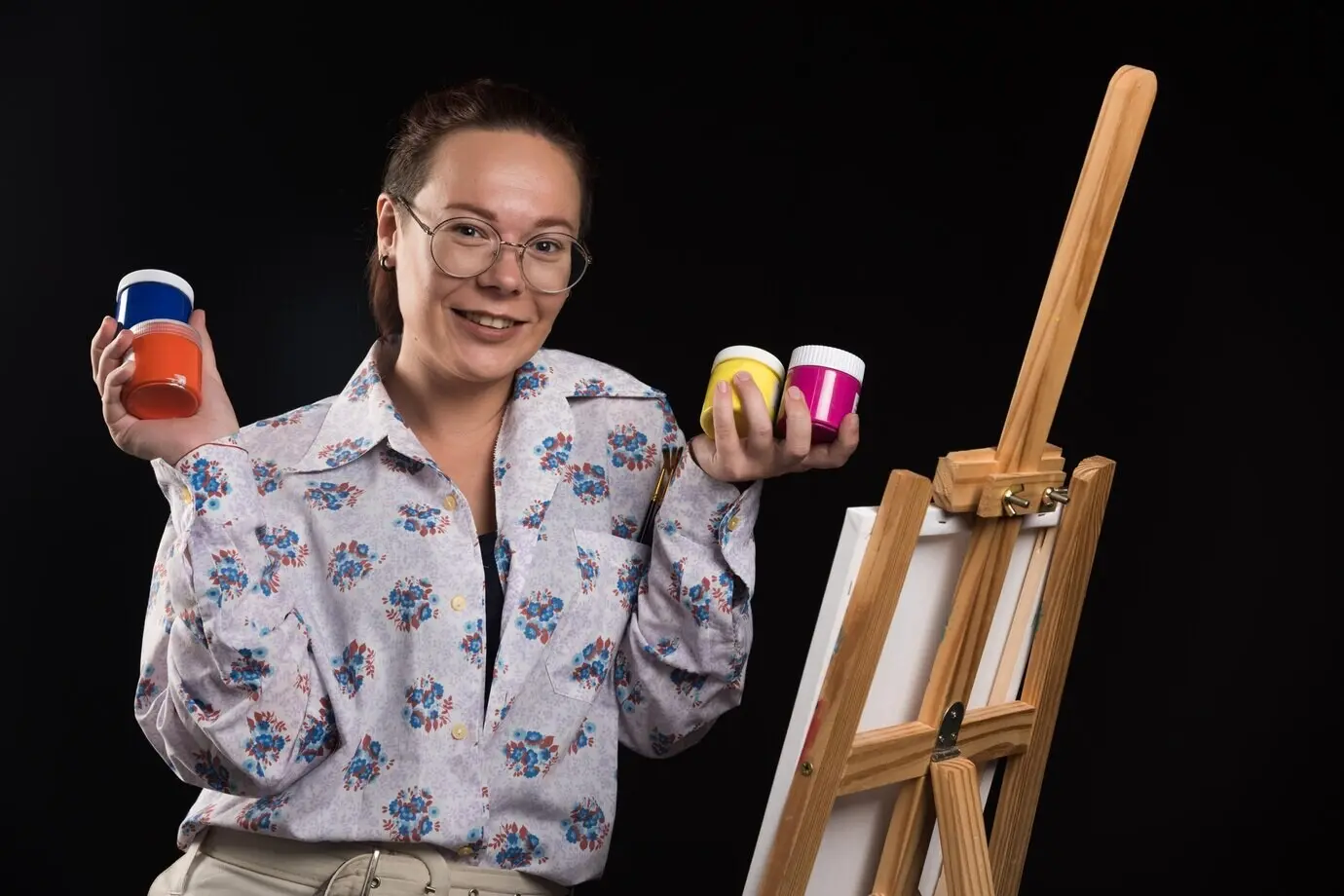 Eine Frau hält einen Pinsel und malt vor schwarzem Hintergrund.