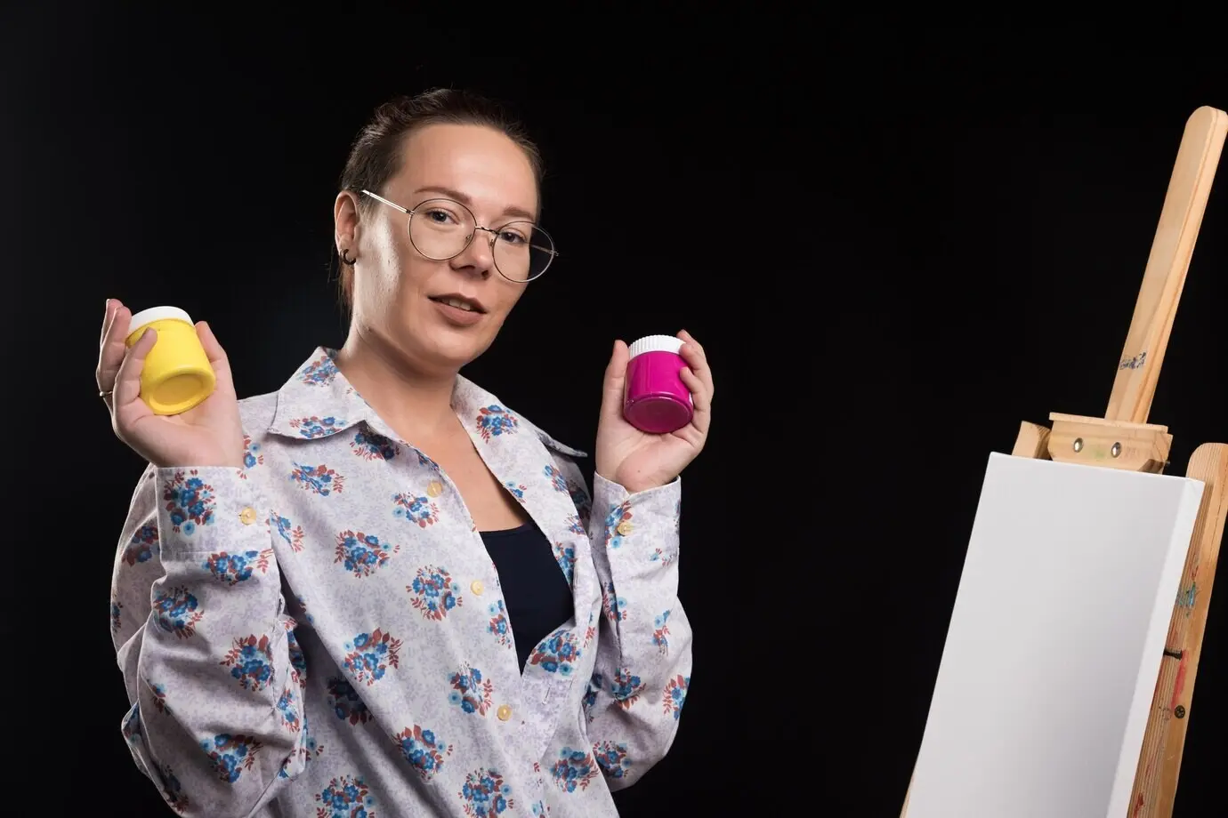 Eine Frau hält einen Pinsel und malt vor schwarzem Hintergrund.