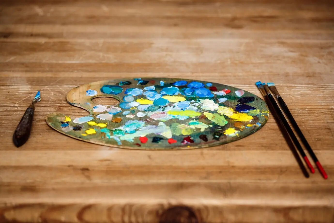 Eine Palette mit Ölfarben und Pinseln über einer Holzwand.